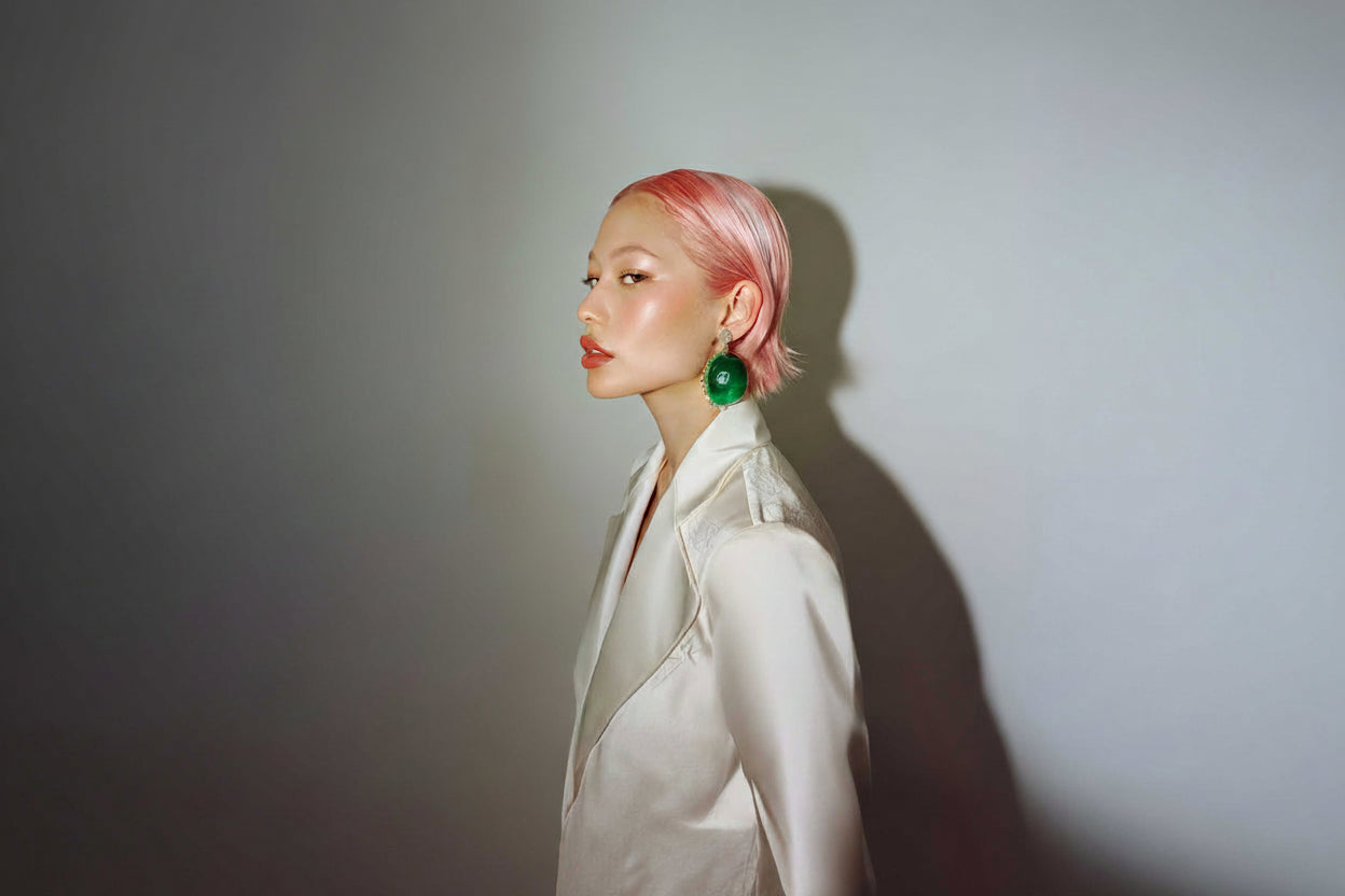 Woman with pink hair wearing a white outfit against a gray background 